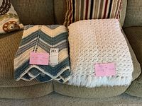Two folded knitted afghans on a couch, one multicolor chevron and one solid white.