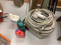 Bissell power steamer with attached power cord coiled on top and flexible hose, plus three bottles of varied floor cleaning solutions in different colors (white, green, red) placed beside it on a wooden surface.