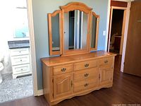 Front view of the wood dresser with metal handles and tri-fold mirror mounted on top showing overall condition and style.