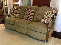 Front view of three-seat reclining sofa with three throw pillows on carpet and wood floor
