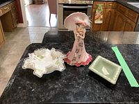 Photo of the three items together on kitchen counter: Wedgwood square dish, Bradford pink dressed figurine, Fenton ruffled bowl