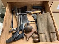 Drawer view showing assorted hand tools including saws, hand drills, wooden handled chisels, and wire brush.