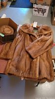 Light brown mink fur coat laid out flat showing texture and included matching fur hat in box