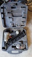 Porter Cable pneumatic nailer in black plastic carrying case with compartments, showing the tool and accessories inside.