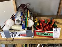 Two boxes, one labeled 'PAINT SUPPLIES' containing paint rollers with foam covers and caulking tubes; the other labeled 'CUTTERS' containing multiple cutting tools such as snips and utility knives with various colored handles.
