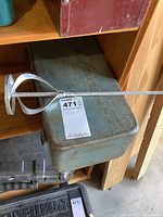Hand-held paint mixer in a storage area next to metal boxes and tools.