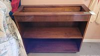 Wooden planter box shelf unit with two storage shelves, dark stained wood, rectangular planter box on top, scratches and scuffs visible