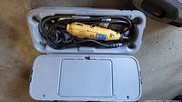 Power Fist yellow rotary tool inside grey plastic case with cord coiled and some accessory bits visible.