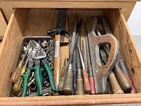 View of drawer containing assorted hand tools including snippers, hammer, chisels, screwdrivers, coping saw frame, and fasteners.