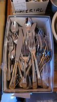 Box holding multiple pieces of stainless steel flatware including forks, spoons, knives in matching pattern
