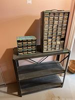 Steel shelf unit holding two hardware organizers with multiple drawers containing various nuts and bolts.