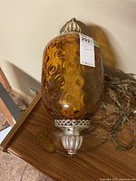 Photo showing the amber glass swag lamp upright with silver-tone metal decorative accents and chain attached.