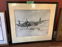 Framed black and white photograph of a De Havilland Mosquito airplane in flight above clouds, showing the full frame and photo within the matte.