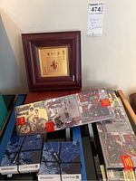 Photo of the framed Asian art print with a dark reddish-brown wooden frame and four packaged Malaysian-themed coasters including 'Street Art Penang' designs and blue Amsterdam United map coasters tied with black ribbons.