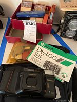 Fuji DL-400 Tele camera placed with original manual, yellow cleaning kit, and a red box containing multiple camera filters and a blue oval Hama filter case.