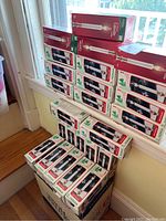 Stacked boxes of NOMA electric candle lamps, showing multiple units piled on a box by a window.