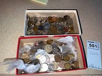 Two boxes containing a large number of mixed foreign coins of various sizes and metals on a countertop.