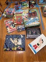 Top view of the lot showing comic books including Captain America, Batman, Godzilla, Mosaic, Dragon Slayer, plus boxed toys including Astro Boy figure, plush, die-cast Stratofortress model and Jetfighter model.