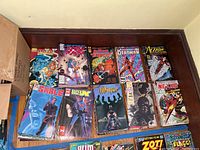 Top view of approximately 12 comic books laid out against a dark wood surface with visible titles including Sable, Racer X, Whisper, Deadman, Cross Roads, Nexus, and Action Comics Weekly