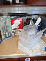 Photo of entire lot showing hardwood knife storage block box, Campagnolo wine opener in packaging, grilling rack, stainless steel bowl, plastic bowls, plastic food storage containers, and marble cheese board.