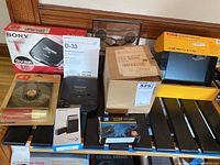 Overview image of all lot items arranged on wooden surface showing boxed Sony Discman D-131, Kodak digital photo frame, microSIM cutter, coin holder, and additional boxed items.