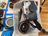 Plastic bin with Leica Digilux camera body, wrist strap and spare lens cap in blue box