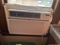 Full view of LG window air conditioner installed in window, showing front grille and vents.