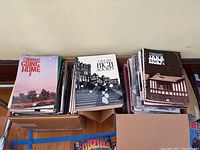 Three cardboard boxes containing trade paperback volumes and stacks of loose magazines: Going Home 7, High Society 2, Jaka’s Story 6 visible on top.