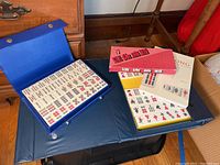 Photo showing two blue Mah Jong game cases containing game tiles and a Mah Jong instruction book on a blue folding mat.
