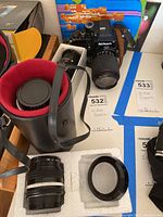 Nikon camera body, lens case, additional lens, and lens adapter on a table surface showing the lot contents.