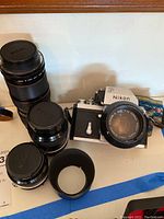 Overview of camera body, three lenses, strap, hood on surface