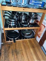 Full view of wooden shelf loaded with kitchen pots and pans, showing construction and paint marks on side edges