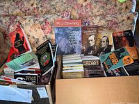 Wide view of the lot with multiple Sherlock Holmes paperback books displayed on floral sofa and inside two boxes