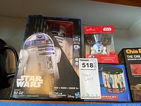 Photo showing original boxed Star Wars R2-D2 robot toy, Hallmark Star Wars R2-D2 ornament, Star Trek transporter mug with Star Trek characters, and a chia pet box labeled 'The Child'.