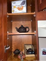 Wooden cabinet shelf showing boxed glass teapot and three clay teapots on lower shelves