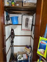 Corner closet space showing Shark vacuum upright and attachments, a blue plastic bucket, various boxes including lightbulbs and tissues