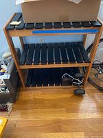 Front view of the wooden three-tier shelf with black slats, showing contents and floor beneath.