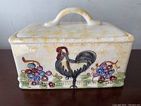Front view of rectangular ceramic bread box showing the painted rooster and grape motif with yellow speckled glaze.