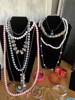 Costume jewelry displayed on black necklace busts and a wooden surface showing various necklaces, bracelets, and earrings in mixed colors and styles.