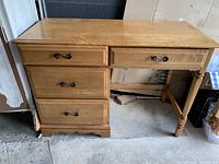 Front view of the wood desk showing four drawers with metal handles and wood finish, with visible wear.