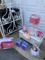 Photo of white iron twin bed frame pieces along with white wooden trunk, metal Eiffel Tower lamp, pink piggy bank, unicorn Easter basket, Disney princess Christmas stocking, two small shelving units, and a twin comforter.
