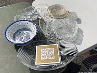 Photo showing several glass platters and dishes, a variegated ceramic bowl with grape motif, and two ceramic tiles with tree illustrations.