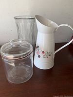 Lot showing all three items together: clear glass canister with lid, tall glass vase, white Disney metal flower vase.