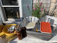 Overview of metal baking pans (including 3-tiered cake pans, loaf pans), yellow Tupperware bowl, wooden salt and pepper shakers
