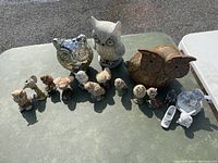 Front view of the table with all owl figurines and additional decorative pieces arranged in daylight on a green table