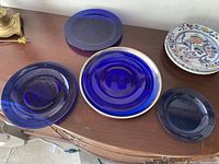 Five blue glass plates and a ceramic plate with floral and bird motifs on a wooden surface