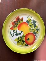 Top view of the round metal platter with painted fruit design and greenish-yellow rim on wooden surface.