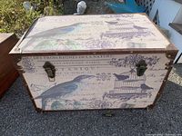 Closed view of the fabric-covered trunk showing bird and vintage script print with metal corner reinforcements and latches.