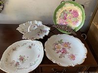 Four vintage porcelain dishes displayed on wood surface showing floral patterns and different shapes