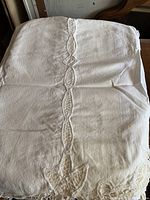 White embroidered mantle scarf with lace trim, folded and laid flat showing central embroidered pattern.